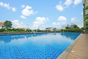 A swimming pool with a wooden deck, surrounded by greenery and buildings in the background. - Asriya by Kozystay - Paskal (Bandung)