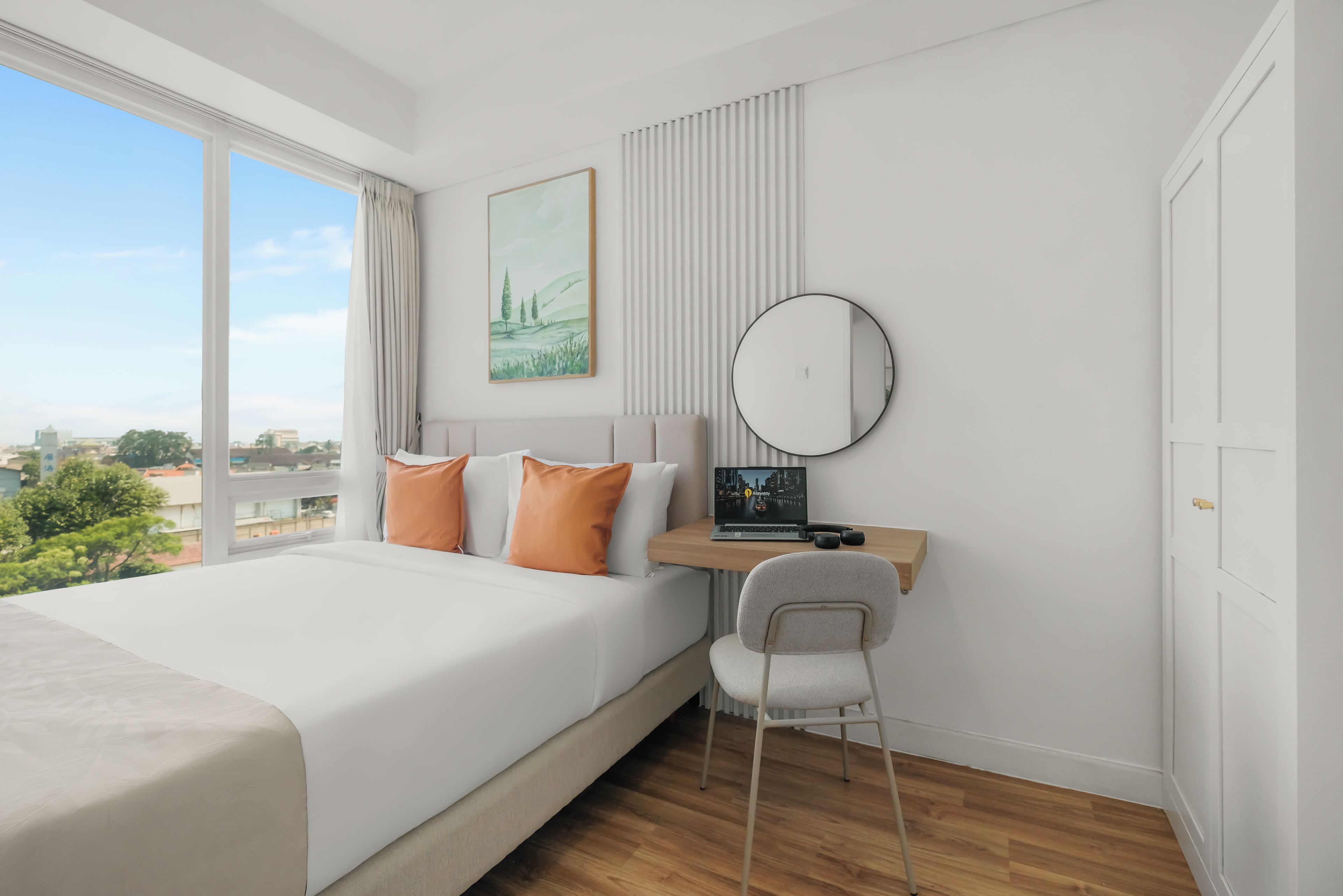 Una habitación de hotel moderna con una cama grande, un escritorio con una computadora portátil, una silla y vistas a la ciudad.