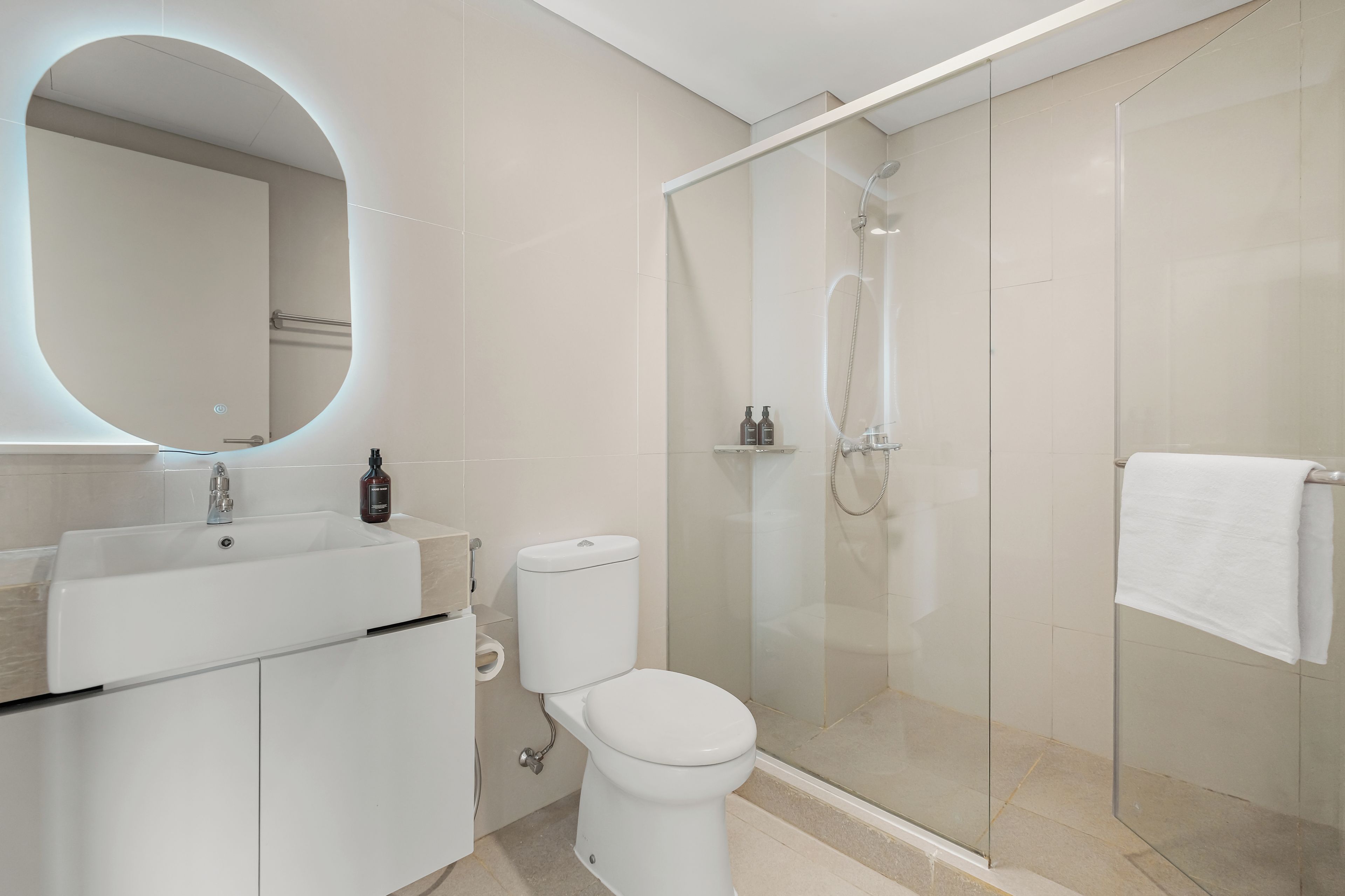 Un baño moderno con ducha envuelta en vidrio, inodoro blanco y lavamanos con espejo.