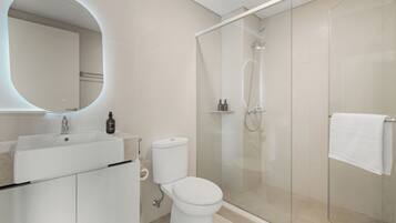 Un baño moderno con ducha envuelta en vidrio, inodoro blanco y lavamanos con espejo.