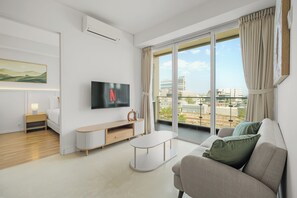 A modern living room with a flat-screen TV, a sofa, a coffee table, and a large window with curtains. - Asriya by Kozystay - Paskal (Bandung)