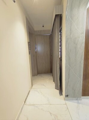 A hallway with a marble floor, a wooden door, and a wall with a marble pattern. - Hotel PLAN SKY (Ahmedabad)