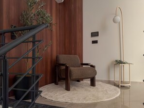A modern interior with a wooden wall, a staircase, a round rug, a brown chair, a tall floor lamp, and a potted plant. - Qoople Elize 68 - 2-bedroom Duplex in Alanya (Alanya)