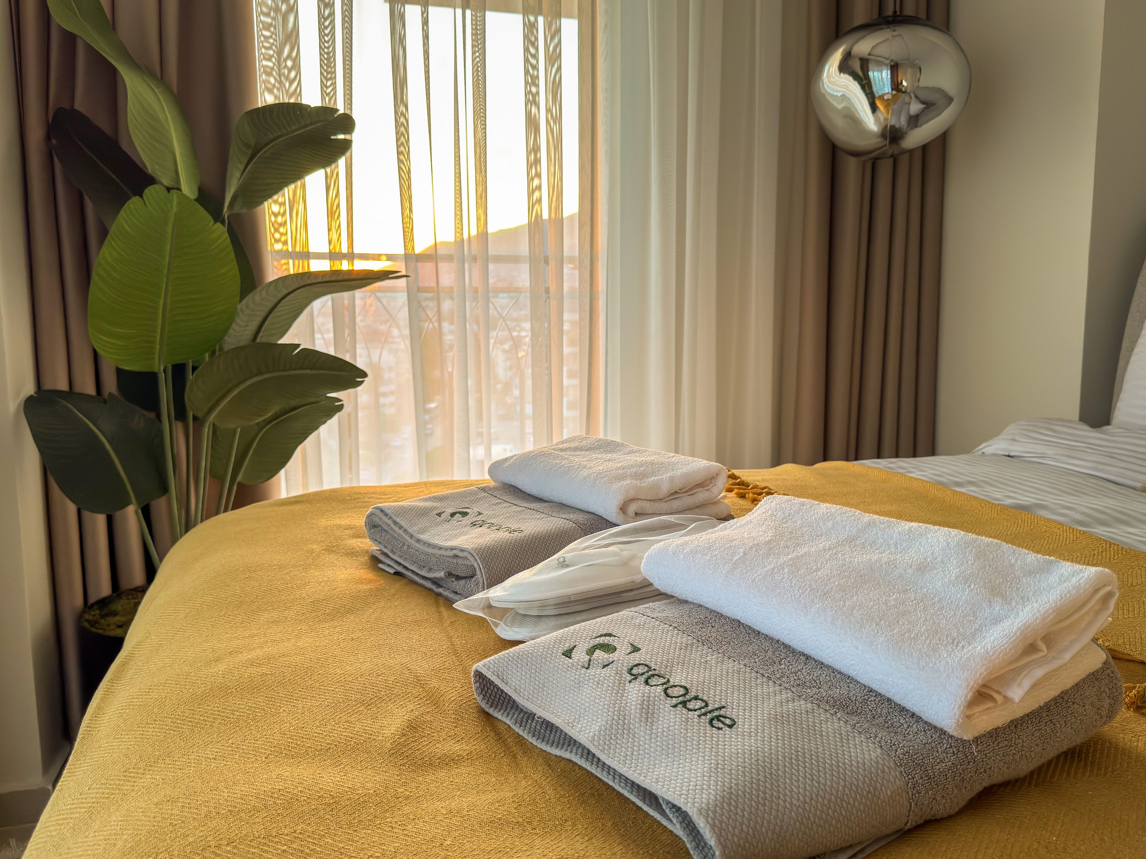 A neatly made bed with a yellow bedspread, a large potted plant, and a mirror on the wall.