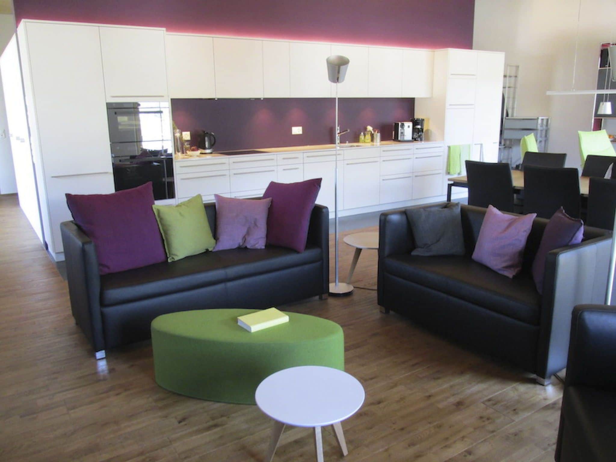 Ein stilvoller Wohnbereich mit zwei Sofas, einem grünen Hocker und einem kleinen weißen Tisch.