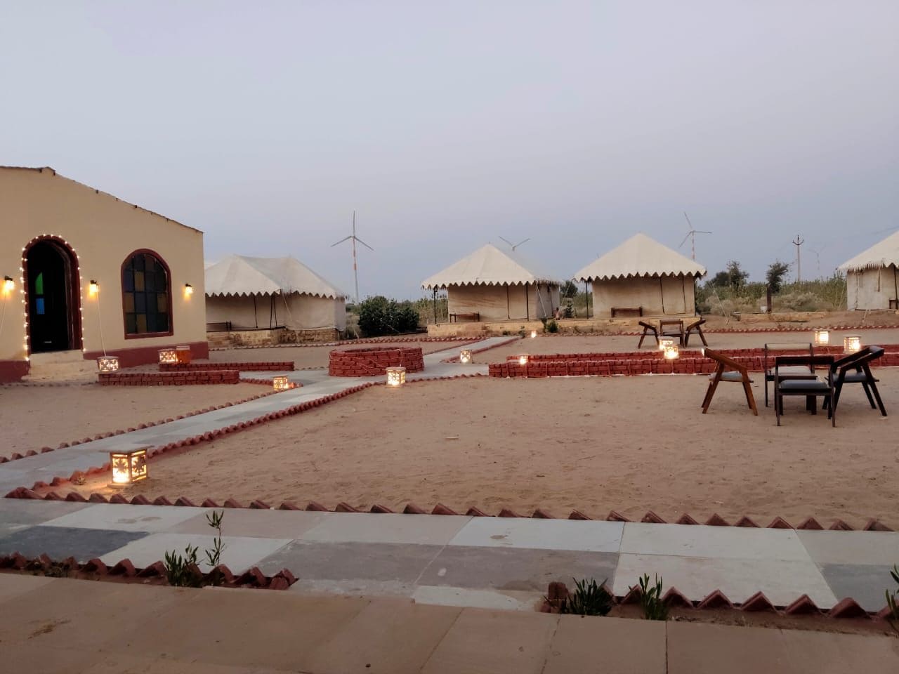 Um resort no deserto com várias cabanas de palha, áreas de estar ao ar livre e um caminho pavimentado.