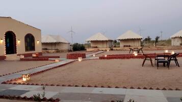 Um resort no deserto com várias cabanas de palha, áreas de estar ao ar livre e um caminho pavimentado.