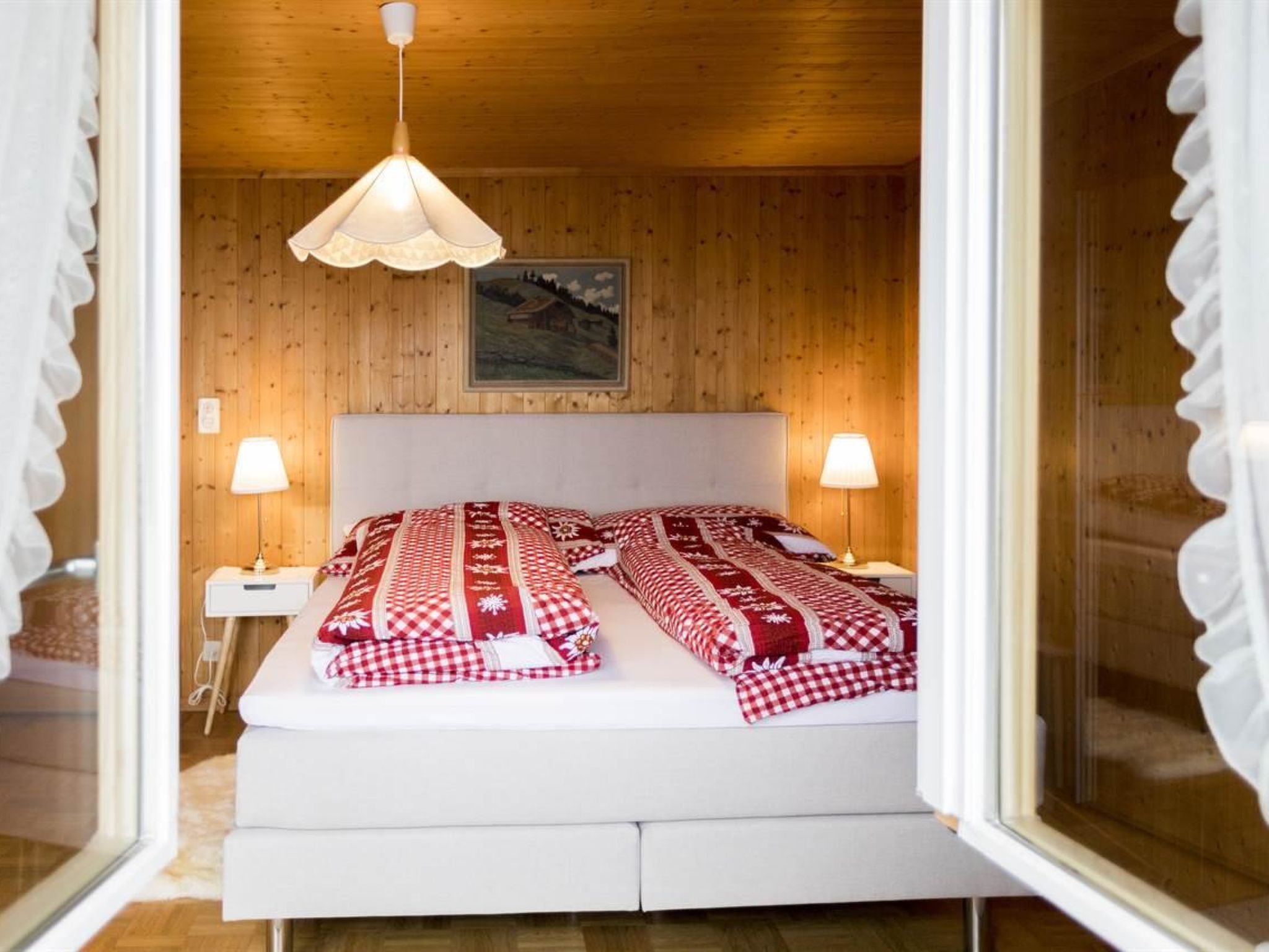 Une chambre avec un lit, deux lampes de chevet, un luminaire suspendu et un tableau encadré au mur.
