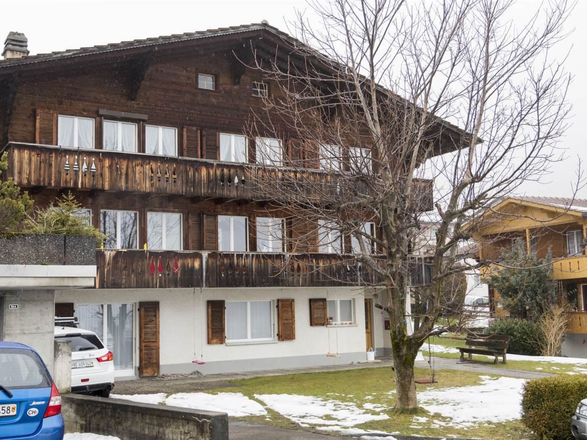 Un immeuble à plusieurs étages, doté d’une façade en bois, de balcons et d’un arbre au premier plan.