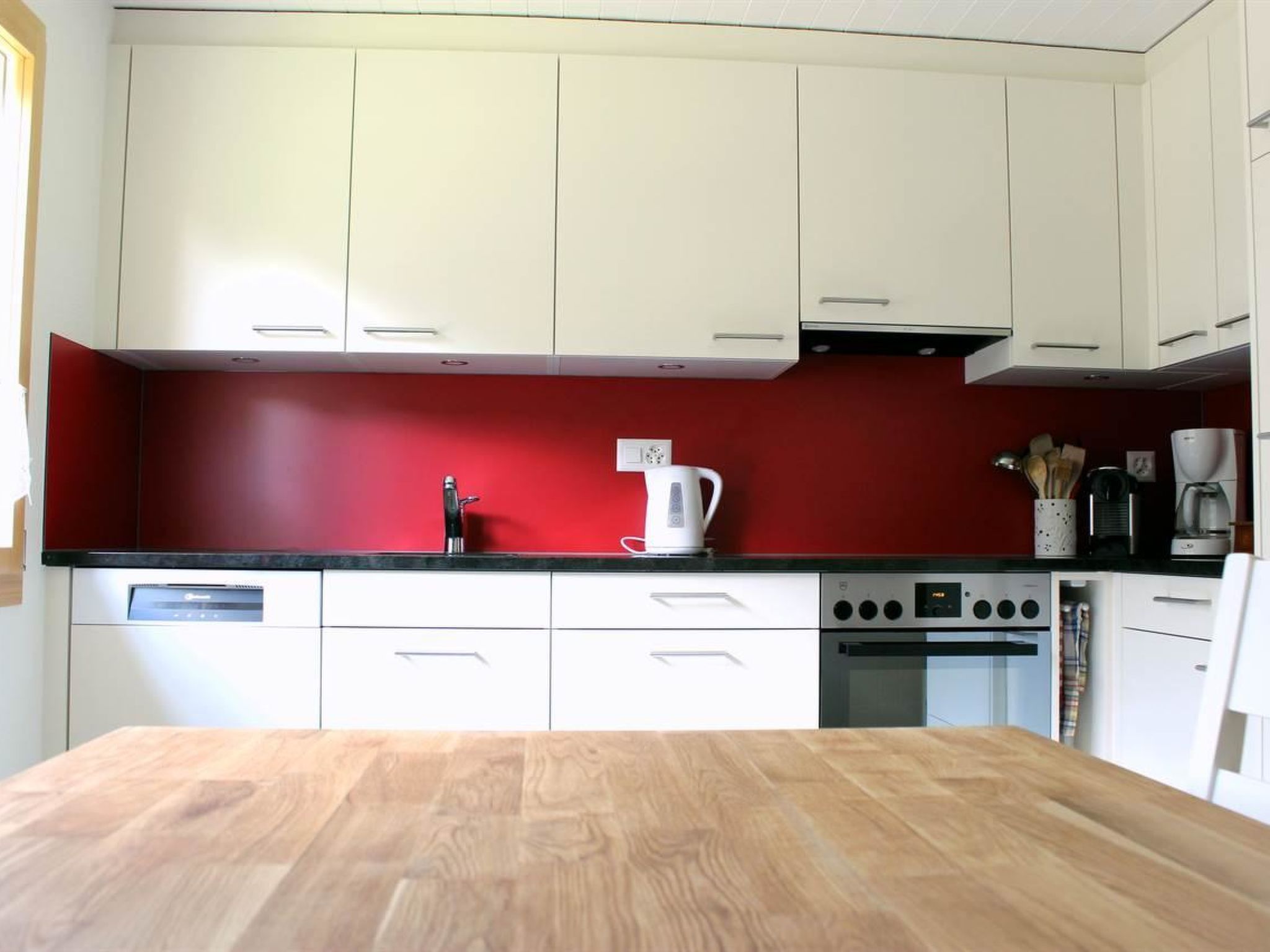 Une cuisine avec des meubles blancs, un pare-feu rouge et un plan de travail en bois.