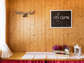 Eine Holzwand mit einem Willkommensschild, ein Tisch mit weißer Tischdecke und eine Blumenkomposition.
