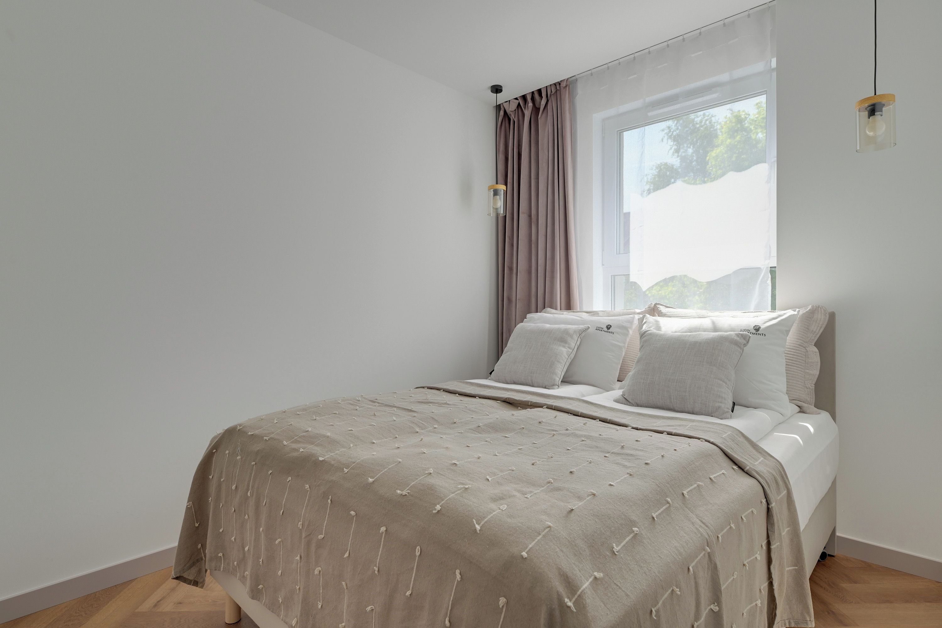 A bedroom with a bed, a window with curtains, and a wall-mounted light fixture.