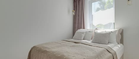 A bedroom with a bed, a window with curtains, and a wall-mounted light fixture.