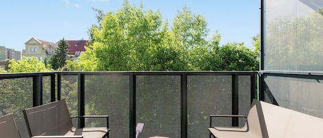 A rooftop terrace with a table and chairs, a mesh screen, and a view of trees and buildings.