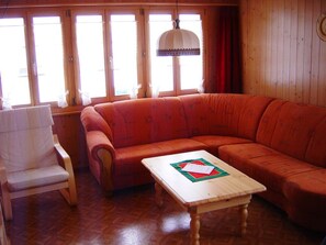 Una habitación con piso de madera, un sofá rojo, una silla blanca y una mesa con papeles.