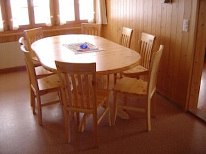 Una mesa de madera redonda con seis sillas, un posavasos y un objeto azul sobre la mesa.
