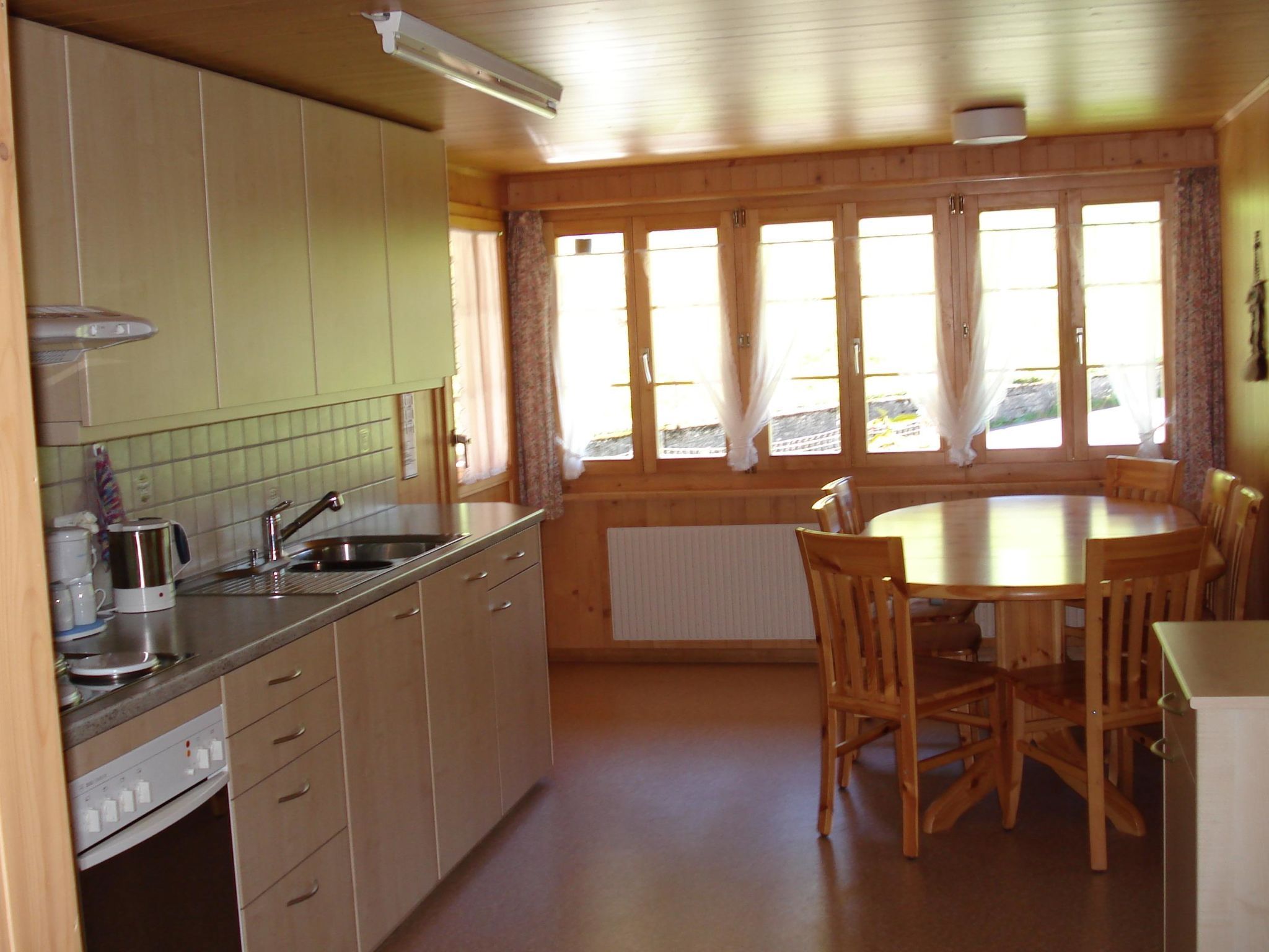 Une cuisine compacte avec un coin repas, des meubles en bois, un four encastré et une fenêtre avec des rideaux.