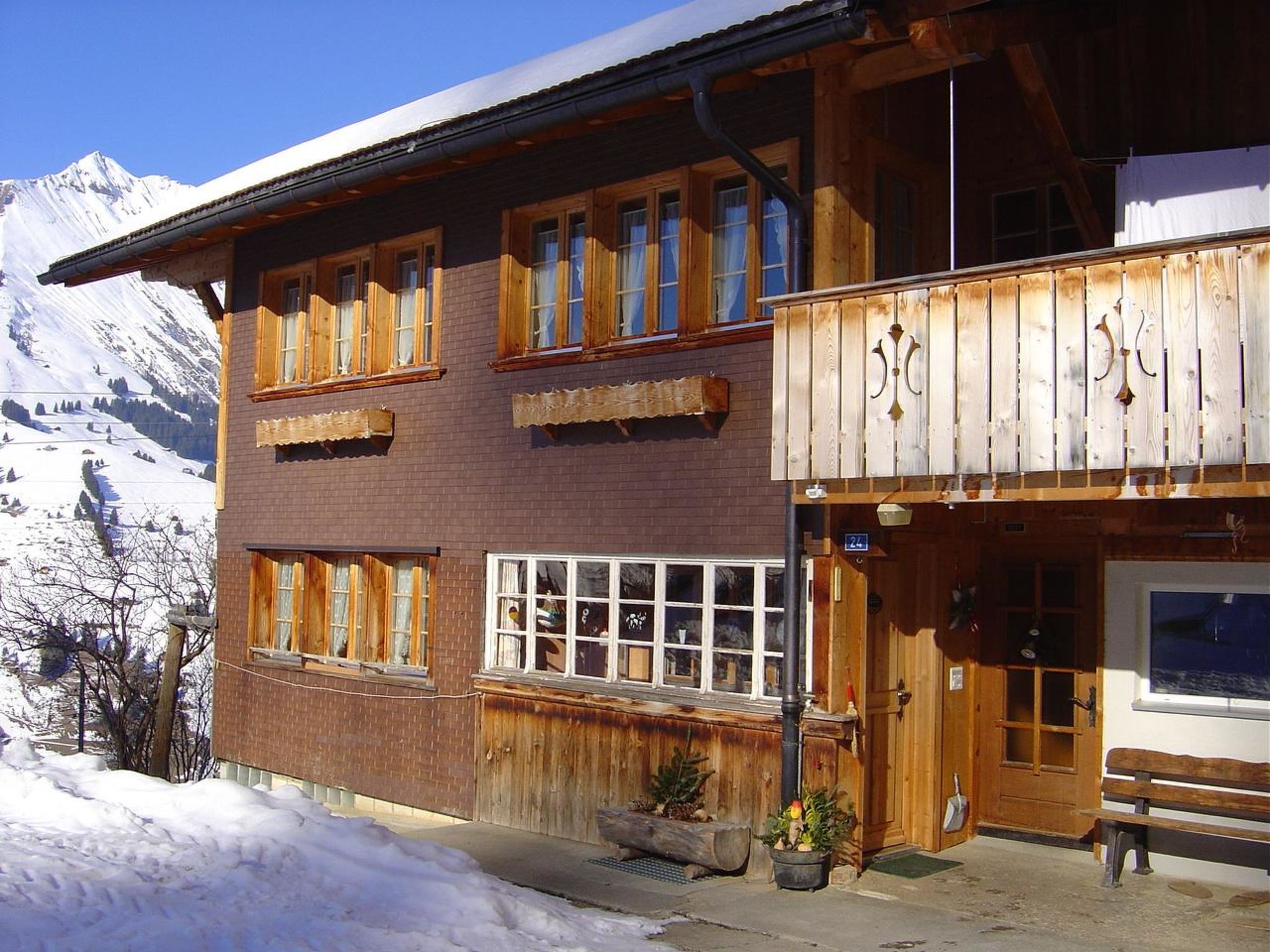 Ein hölzernes Gebäude mit mehreren Fenstern und einem Balkon, vor einer verschneiten Berglandschaft.