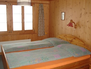 A wooden room with two beds, a window, a curtain, and a wall-mounted lamp.