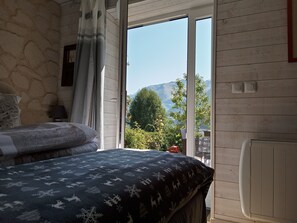 Un dormitori amb llit, una tauleta de nit, una finestra amb vista a les muntanyes i una paret de pedra.
