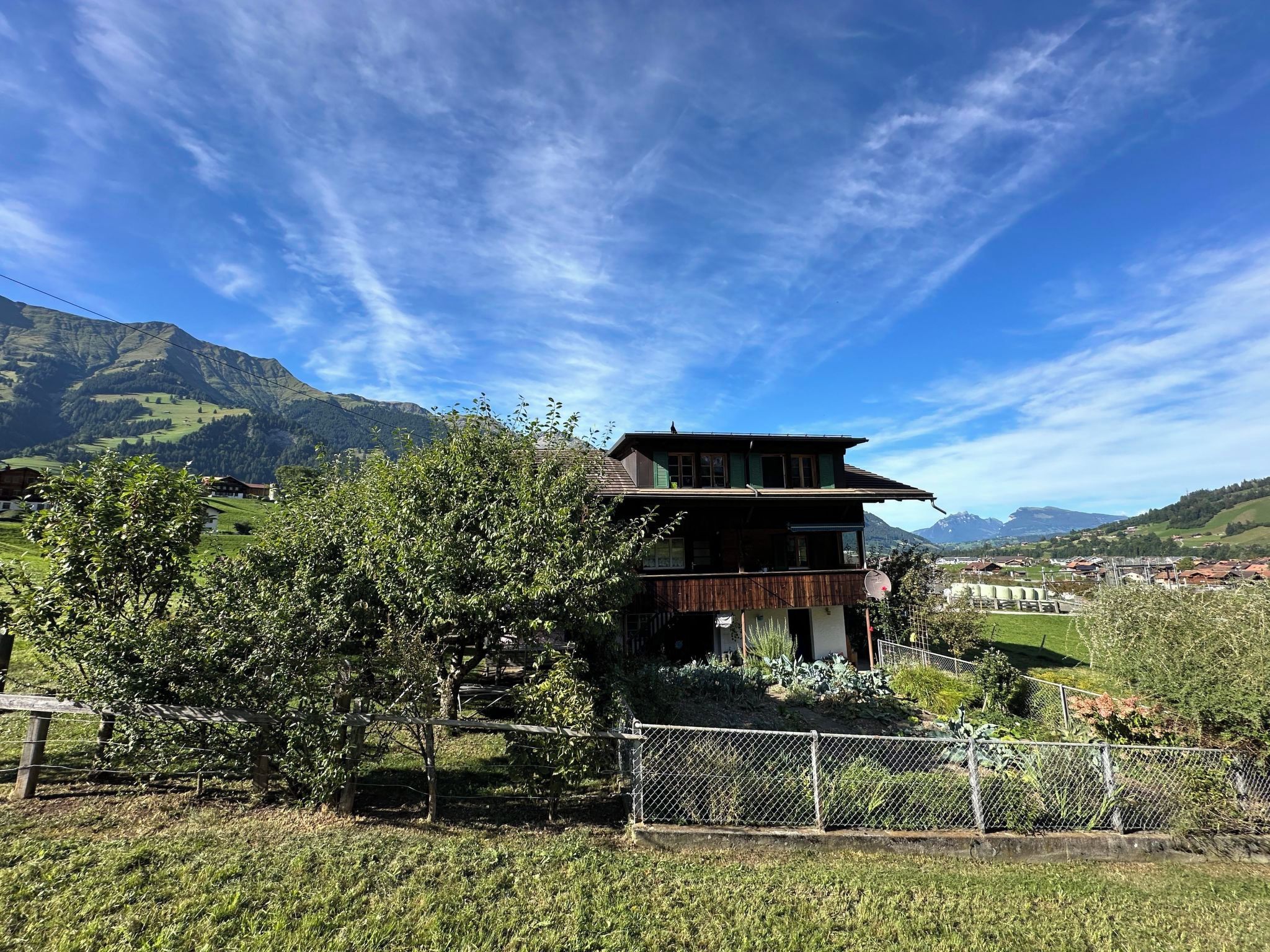 Ein zweistöckiges Gebäude mit Balkon, umgeben von Grünflächen und Bergen im Hintergrund.