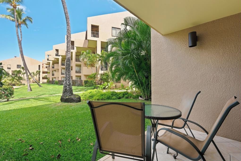 A patio area with a table and chairs, surrounded by a well-maintained lawn and palm trees.