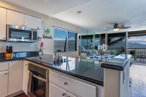 A modern kitchen with a large island, stainless steel appliances, and a view of the ocean. - Maalaea Kai #220- Relaxing 2BR/2BA Oceanfront Maui Condo with Private Lanai, Stunning Ocean Views (Wailuku)