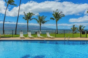 A swimming pool with lounge chairs and palm trees, with a view of the ocean and mountains in the background. - Maalaea Kai #220- Relaxing 2BR/2BA Oceanfront Maui Condo with Private Lanai, Stunning Ocean Views (Wailuku)