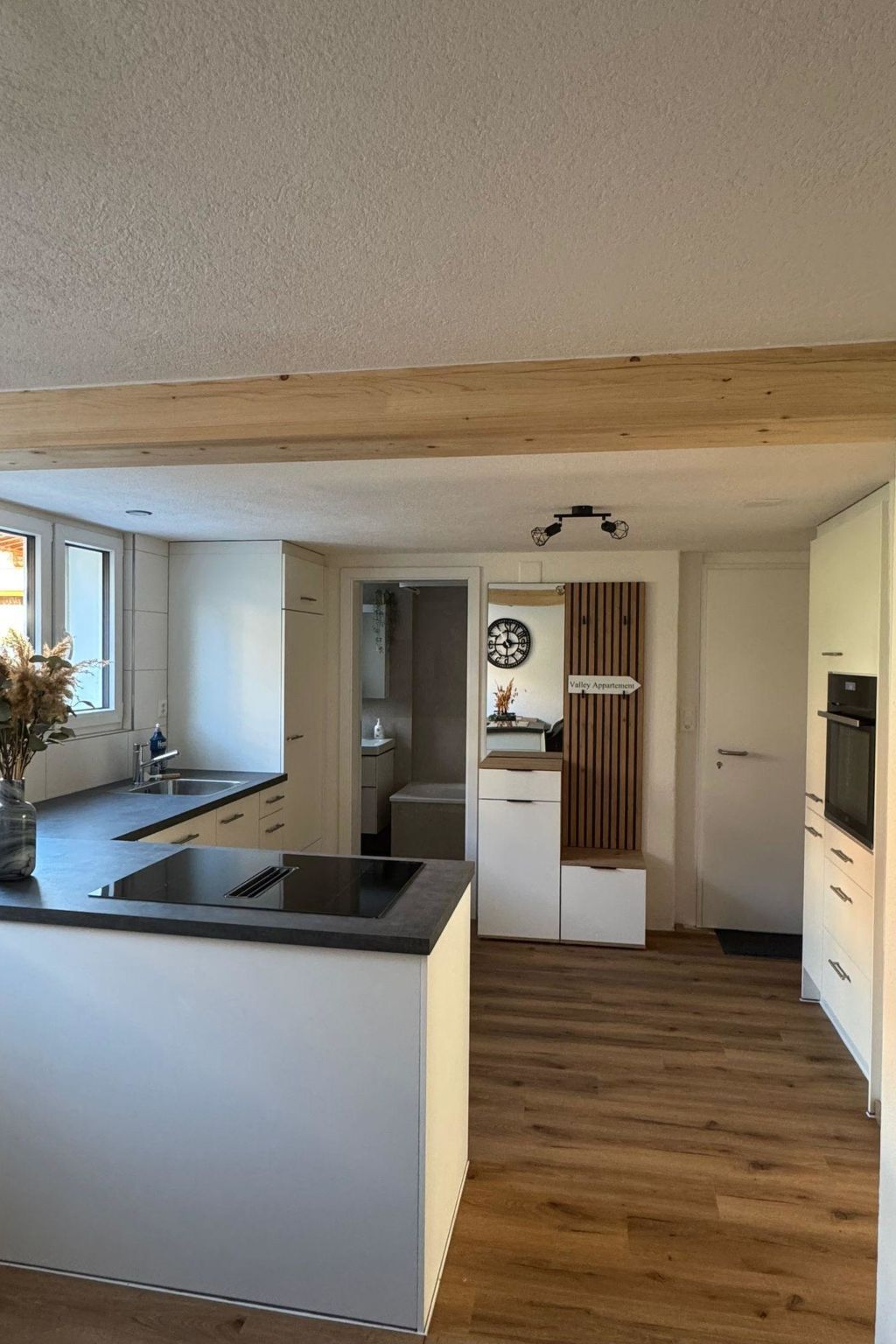 Eine moderne Küche mit einer zentralen Kochinsel, Holzböden und Blick in den Wohnbereich.