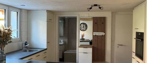 A modern kitchen with a central island, wooden flooring, and a view into the living area.