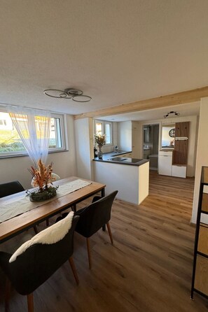 A modern kitchen with a central island, a dining area with a wooden table and chairs, and a view of the living area through an open doorway. - Valley Appartement Appartement/Fewo, Bad, WC, 2 Schlafräume 3 1/2-Zimmerwohnung by Interhome (Frutigen)
