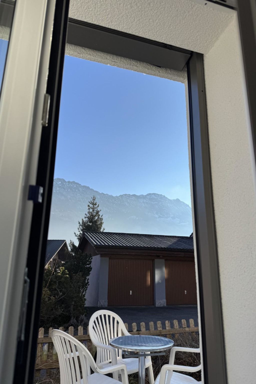 Un balcón con vistas a las montañas, una cerca de madera y una mesa con sillas.