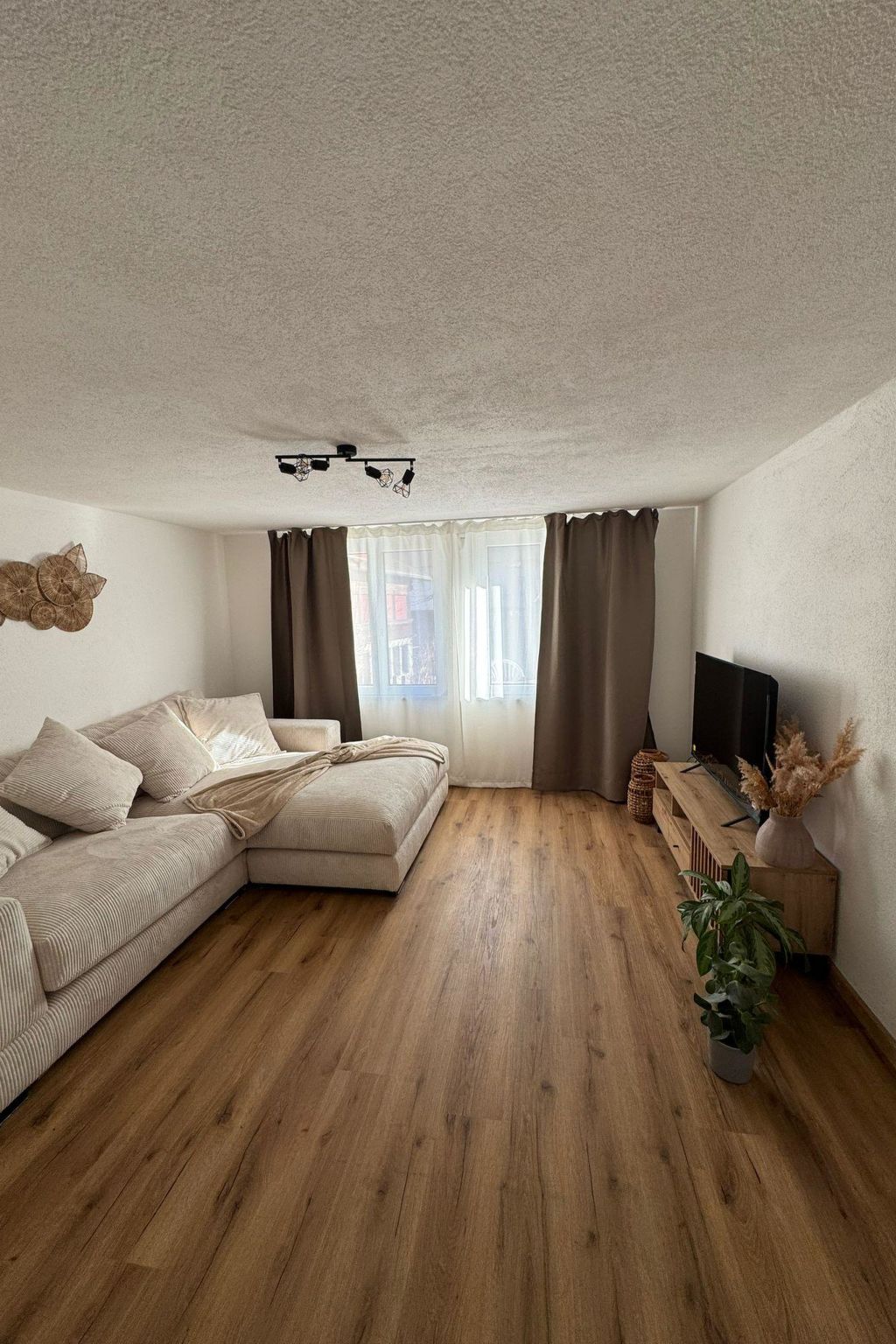 Un salon moderne avec un canapé d’angle, un téléviseur à écran plat et un plancher en bois.