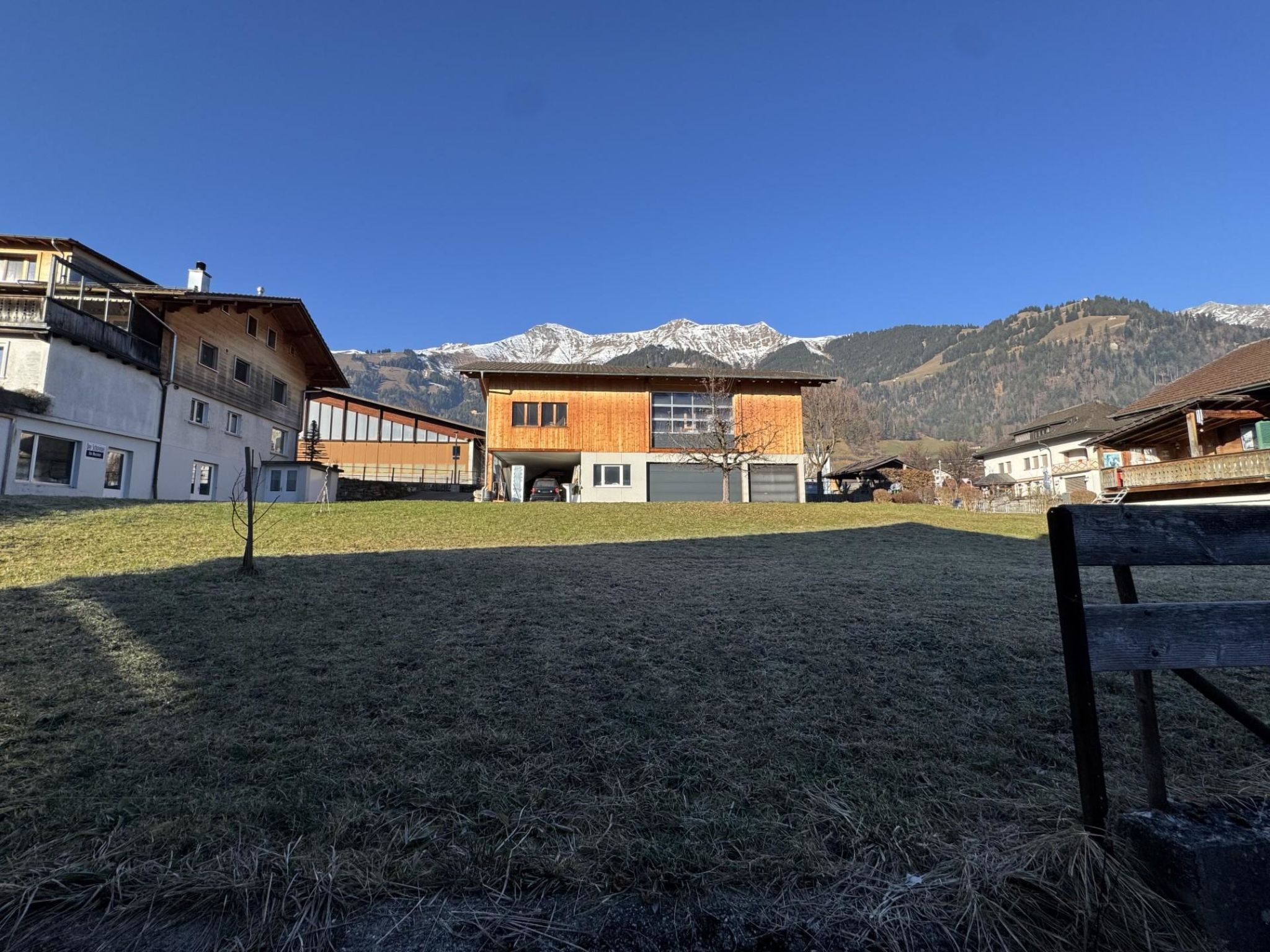 A modern building with a garage, surrounded by a grassy area and mountains in the background.