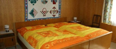 A bedroom with a wooden bed, a quilt, a nightstand, and a wall hanging.
