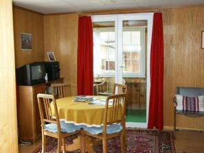 Ein Essbereich mit Tisch, Stühlen, einem Fernseher und Blick durch eine Glastür.
