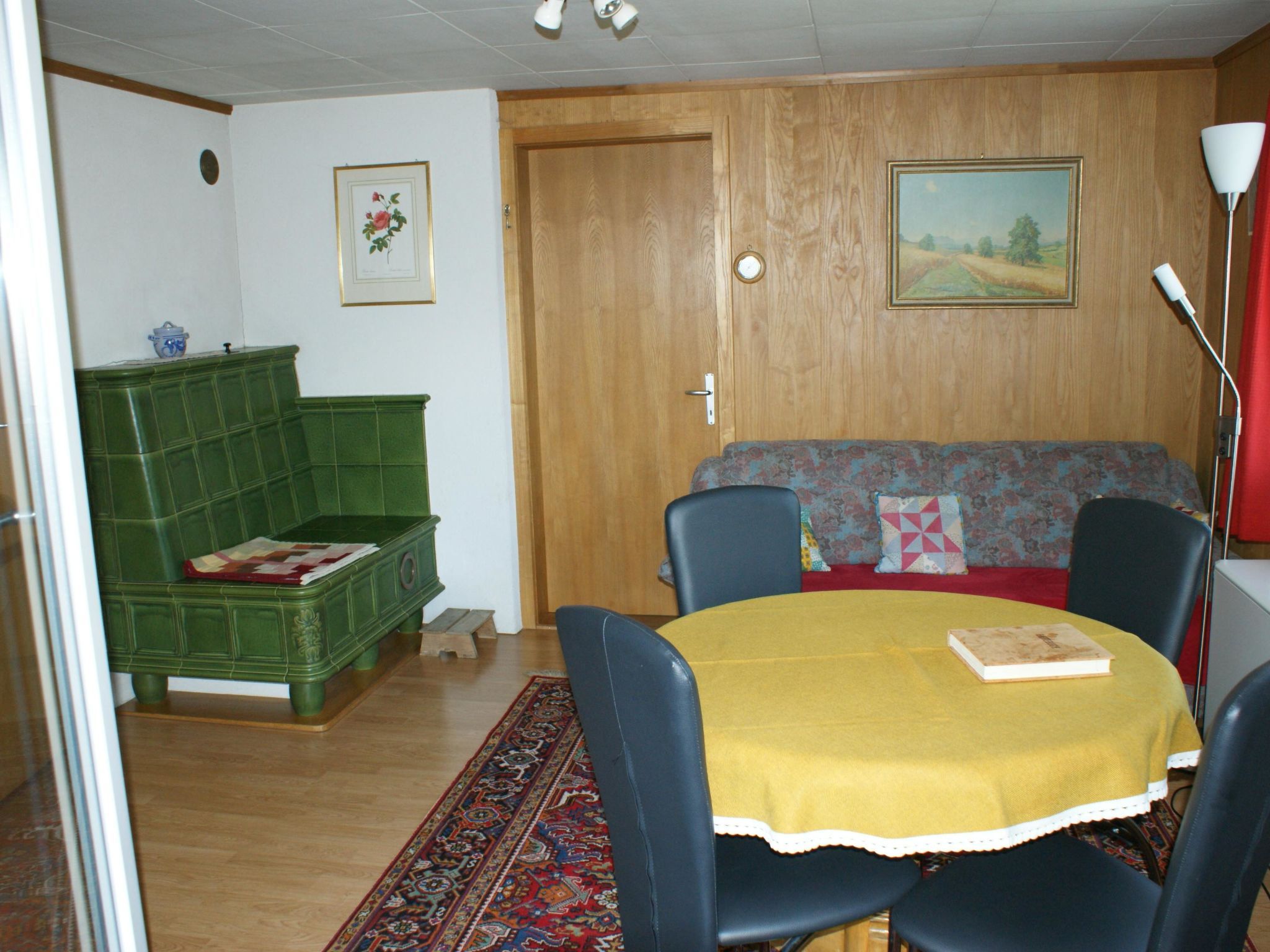 Una habitación con un sofá verde, una mesa amarilla y una puerta de madera.