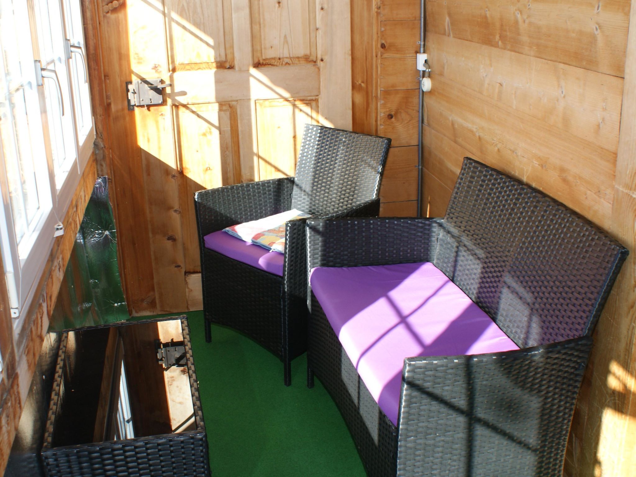 Ein Zimmer mit grünem Boden, einem Korbssessel und einem Stuhl mit violettem Kissen.