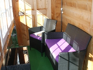 Ein Zimmer mit grünem Boden, einem Korbssessel und einem Stuhl mit violettem Kissen.