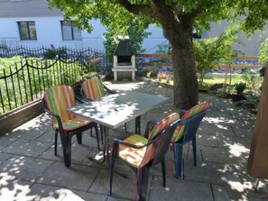 Un patio exterior con mesa y sillas, una parrilla y un jardín cercado.