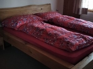 Una cama de madera con colchón rojo y ropa de cama estampada con motivos florales.