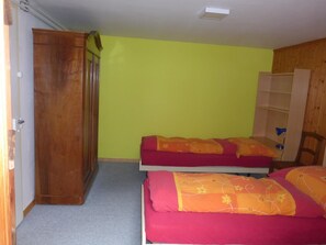 Ein Zimmer mit zwei Betten, einem Holzschrank und einer Regalwand.