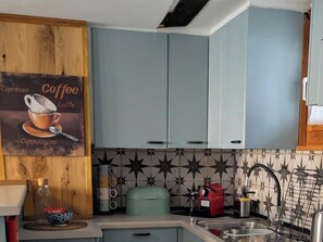 Une cuisine avec des meubles de couleur bleu clair, une décoration murale sur le thème du café, une machine à café et un pare-feu décoratif.