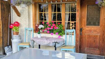 Un chalet en bois avec une table et des chaises en verre, une porte et des jardinières suspendues.