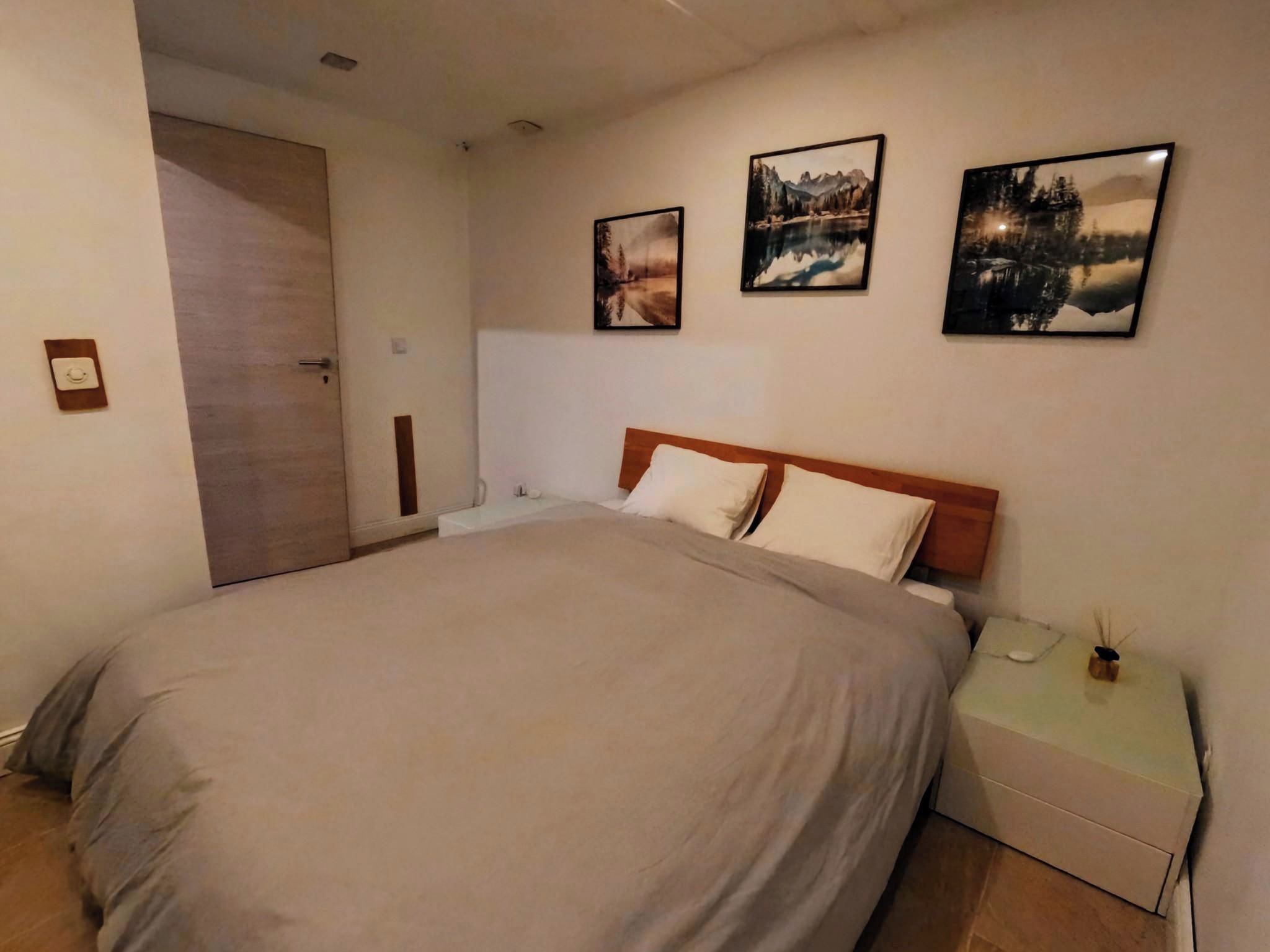 Une chambre à coucher avec un grand lit, une table de chevet et trois tableaux représentant des paysages accrochés au mur.