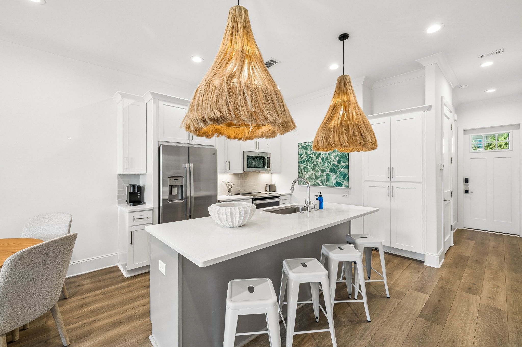 A modern kitchen with a central island, white cabinetry, stainless steel appliances, and a hanging light fixture.