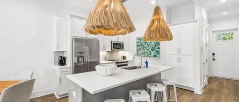 A modern kitchen with a central island, white cabinetry, stainless steel appliances, and a hanging light fixture.