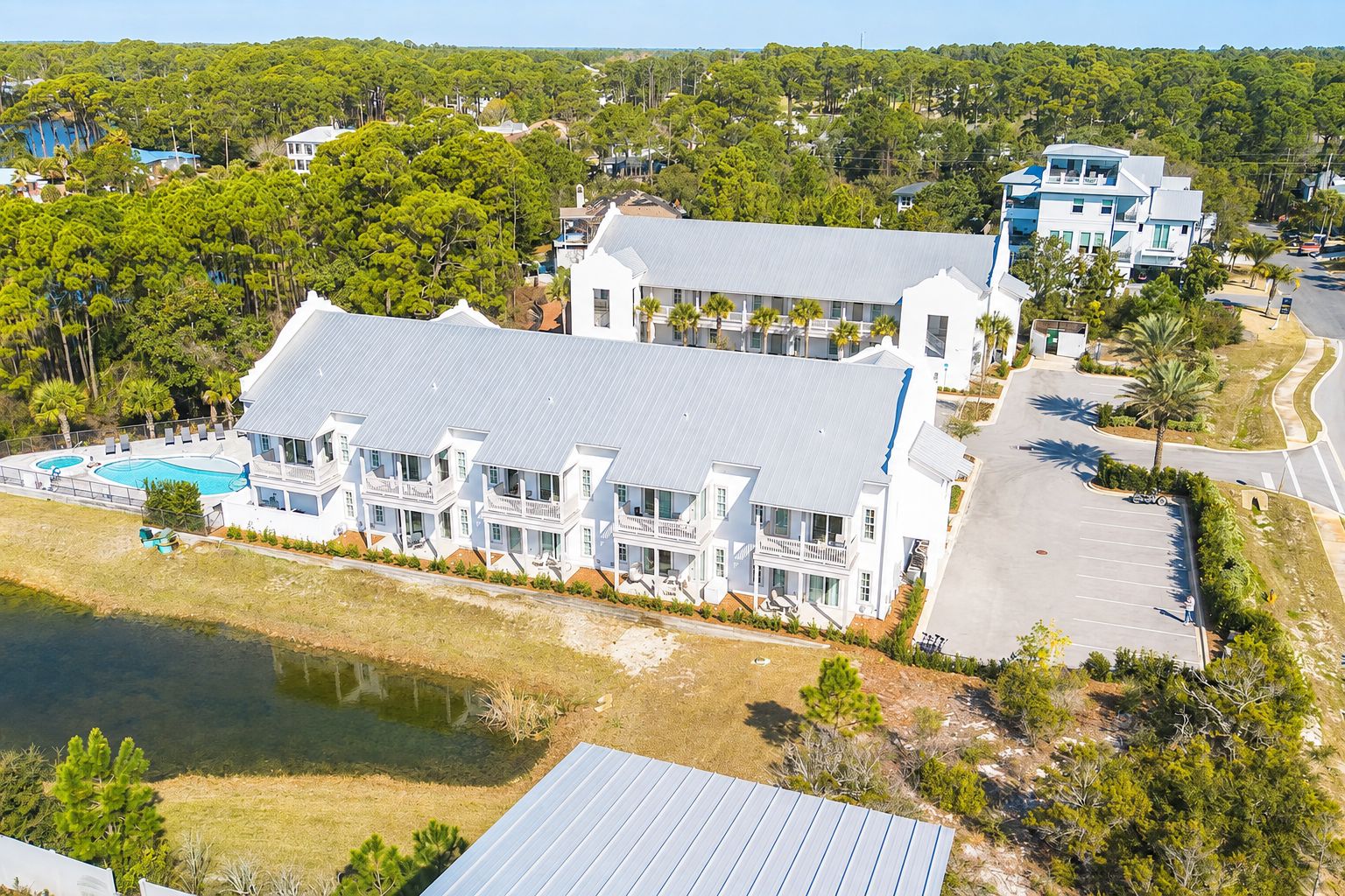 A large white building with multiple balconies, a swimming pool, and a parking area.