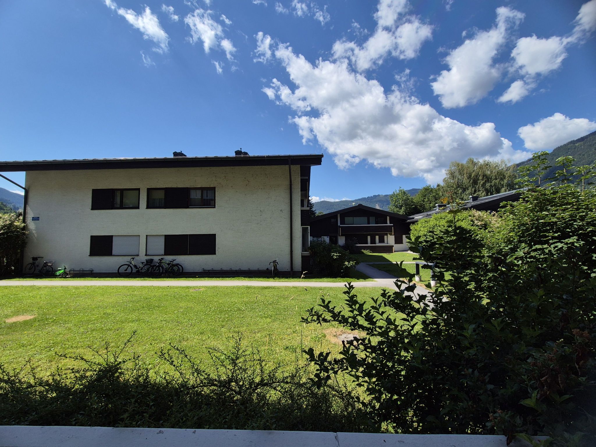 A two-story building with a flat roof, a grassy yard, and a mountain backdrop.