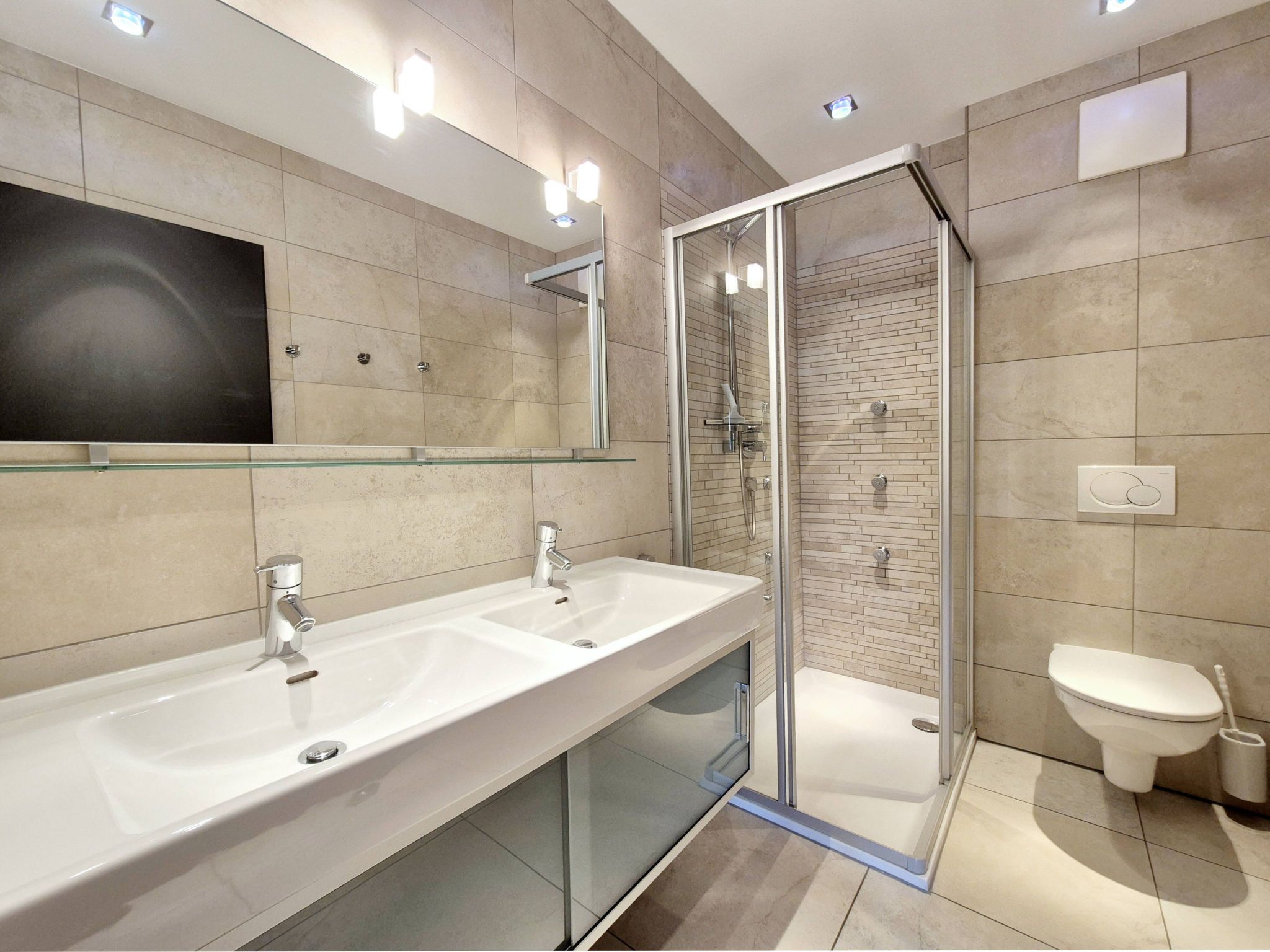 A modern bathroom with a glass-enclosed shower, two sinks, and a toilet.